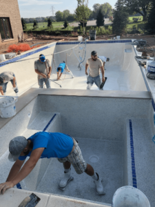 workers standing inside empty pool installation, working on pool surfacing stage