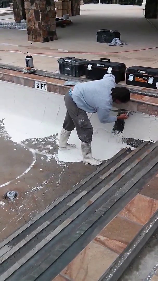 pool construction worker uses trowel to apply Masonite plaster to pool interior